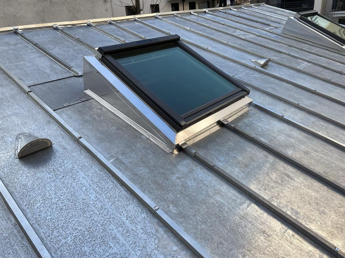 Costière métallique réhaussant une fenêtre de toit sur une couverture zinc à faible pente